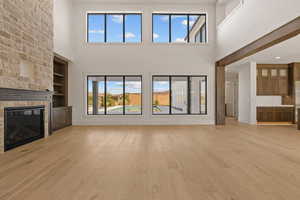 Unfurnished living room with light wood finished floors, a stone fireplace, a high ceiling, built in features, and recessed lighting
