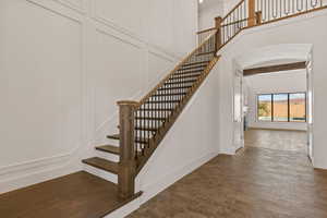 Staircase featuring a decorative wall, a high ceiling, arched walkways, and wood finished floors