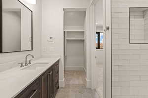 Full bath with light tile patterned floors, vanity, a spacious closet, and tiled shower
