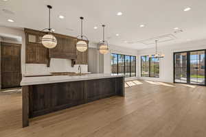 Kitchen with decorative backsplash, decorative light fixtures, recessed lighting, light wood-type flooring, and dark brown cabinetry