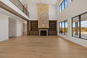 Unfurnished living room with recessed lighting, light wood-style flooring, a large fireplace, a high ceiling, and arched walkways