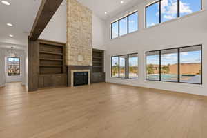 Unfurnished living room featuring recessed lighting, light wood-type flooring, a fireplace, and a towering ceiling