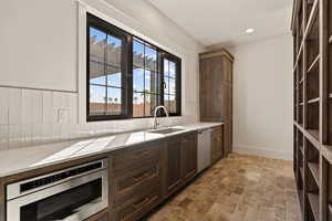 Kitchen with dark brown cabinets, stainless steel oven, backsplash, dishwasher, and recessed lighting