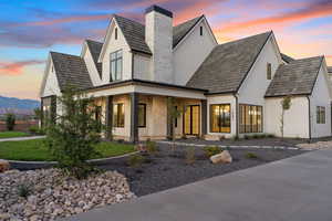 View of front of property with stucco siding, a porch, a chimney, and brick siding