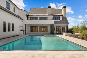 Rear view of house featuring a chimney, a patio area, stucco siding, and a pool with connected hot tub