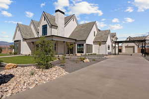 View of front of property featuring a garage, a chimney, driveway, a porch, and an outdoor structure