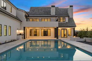 Rear view of house featuring a chimney, a standing seam roof, an outdoor pool, a patio, and a metal roof