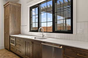 Kitchen with stainless steel appliances, brown cabinetry, and light stone counters