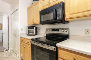 Kitchen with stainless steel range with electric stovetop, black microwave, light countertops, light brown cabinets, and light tile patterned flooring