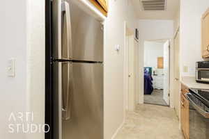 Kitchen with stainless steel appliances, light countertops, light tile patterned flooring, and light brown cabinetry