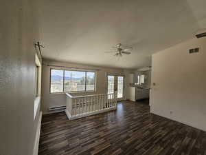 Unfurnished living room featuring french doors, a textured ceiling, dark wood-style floors, baseboard heating, and a ceiling fan