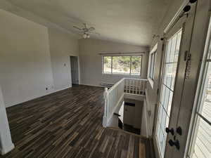 Unfurnished living room with vaulted ceiling, dark wood-style floors, a textured ceiling, and a ceiling fan