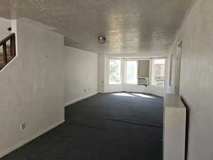 Unfurnished living room featuring a textured wall, a textured ceiling, dark carpet, and cooling unit