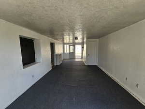 Hallway featuring a textured wall, dark carpet, and a textured ceiling