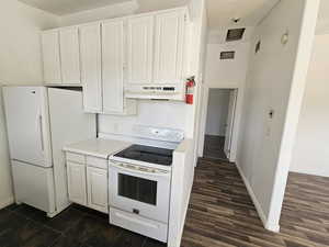 Kitchen with light countertops, white appliances, white cabinets, under cabinet range hood, and dark wood finished floors