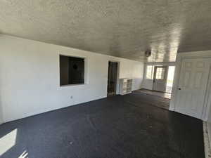 Unfurnished living room featuring a textured wall, a textured ceiling, and dark colored carpet