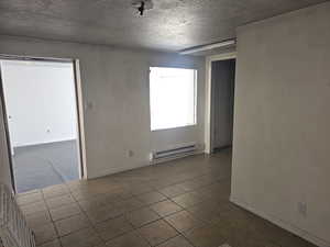 Unfurnished room with a textured ceiling, dark tile patterned flooring, baseboard heating, and a textured wall