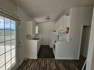 Kitchen with white cabinets, white appliances, dark wood-style flooring, light countertops, and a textured ceiling