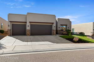View of front facade with driveway, stucco siding, stone siding, and a garage
