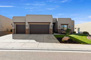 Pueblo-style home with stucco siding, concrete driveway, stone siding, and an attached garage