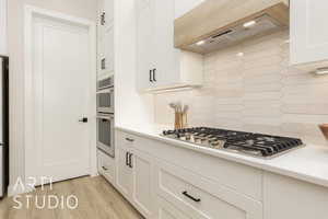 Kitchen featuring backsplash, extractor fan, white cabinetry, stainless steel appliances, and light wood-style flooring