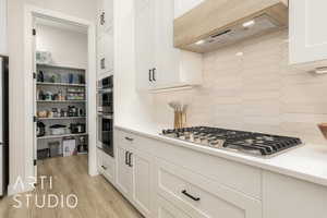 Kitchen featuring tasteful backsplash, ventilation hood, white cabinetry, appliances with stainless steel finishes, and light wood-style floors