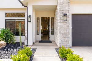Property entrance featuring stucco siding, stone siding, and a garage