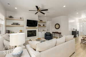 Living room featuring built in shelves, light wood-style flooring, a glass covered fireplace, recessed lighting, and a ceiling fan