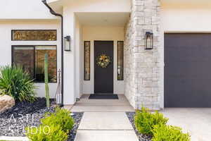 Entrance to property with stucco siding, stone siding, and a garage
