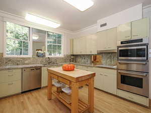 Kitchen with crown molding, dishwasher, light wood-type flooring, decorative backsplash, and light stone counters