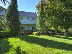 Colonial-style house with covered porch, a front lawn, and a chimney