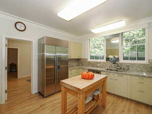 Kitchen with stainless steel appliances, cream cabinetry, light wood-style floors, light stone countertops, and crown molding