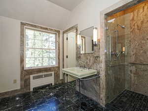 Full bathroom featuring marble tiled floors, a marble finish shower, vaulted ceiling, and radiator