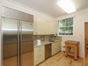 Kitchen with appliances with stainless steel finishes, light wood-type flooring, light stone counters, backsplash, and ornamental molding