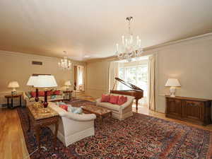 Living area with light wood-type flooring, a chandelier, a decorative wall, wainscoting, and crown molding