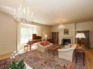 Living room with a chandelier, a decorative wall, light wood-style flooring, a high end fireplace, and ornamental molding