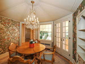 Dining space featuring wallpapered walls, crown molding, a chandelier, radiator heating unit, and wood finished floors