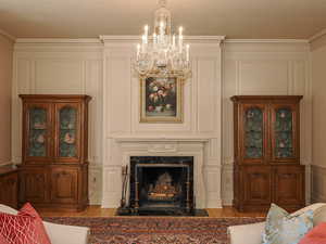Living area with a decorative wall, ornamental molding, a high end fireplace, light wood-type flooring, and a chandelier