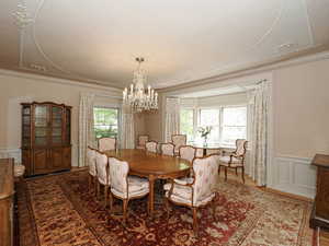 Dining area with a decorative wall, a wainscoted wall, a chandelier, ornamental molding, and wood finished floors