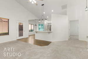 Kitchen featuring dark colored carpet, high vaulted ceiling, decorative light fixtures, a kitchen bar, and a ceiling fan