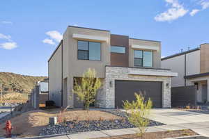 Modern home featuring stone siding, a garage, concrete driveway, and stucco siding