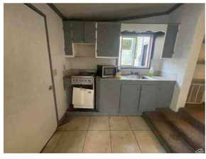 Kitchen featuring gray cabinetry, white stove, light tile patterned floors, crown molding, and stainless steel microwave