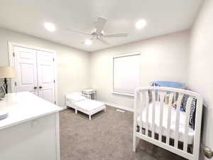 Bedroom with a crib, light colored carpet, ceiling fan, a closet, and recessed lighting
