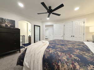 Carpeted bedroom featuring ornamental molding, a closet, a ceiling fan, arched walkways, and recessed lighting