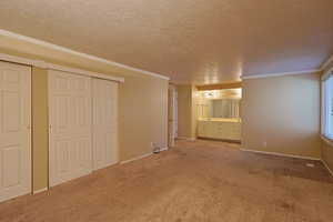 Unfurnished bedroom featuring ornamental molding, light carpet, a closet, a textured ceiling, and connected bathroom
