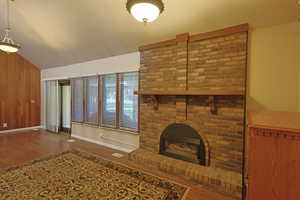 Unfurnished living room with wood finished floors, lofted ceiling, a fireplace, wood walls, and a textured ceiling