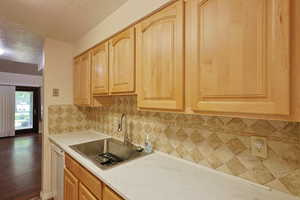Kitchen featuring a textured ceiling, backsplash, light brown cabinets, dishwasher, and light stone counters