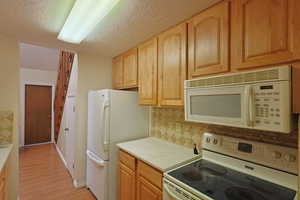 Kitchen with white appliances, tasteful backsplash, light countertops, a textured ceiling, and light wood-type flooring