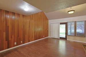Spare room with a textured ceiling, dark wood-style flooring, and wooden walls