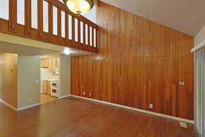 Unfurnished living room with a textured ceiling, wooden walls, a towering ceiling, and dark wood-style floors